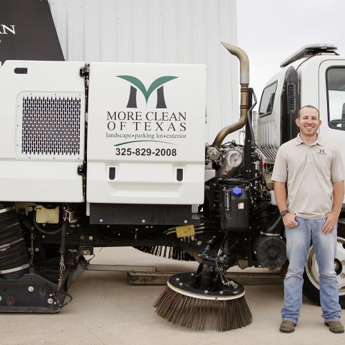 Cole Watts, president of More Clean of Texas standing in front of a More Clean of Texas sweeper truck.