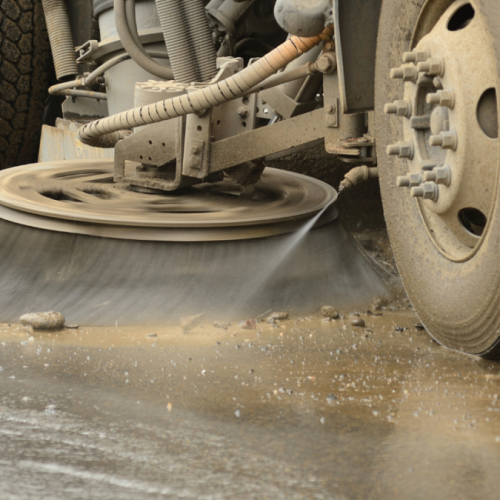 Sweeper truck sweeping up gravel and mud from a paved surface,